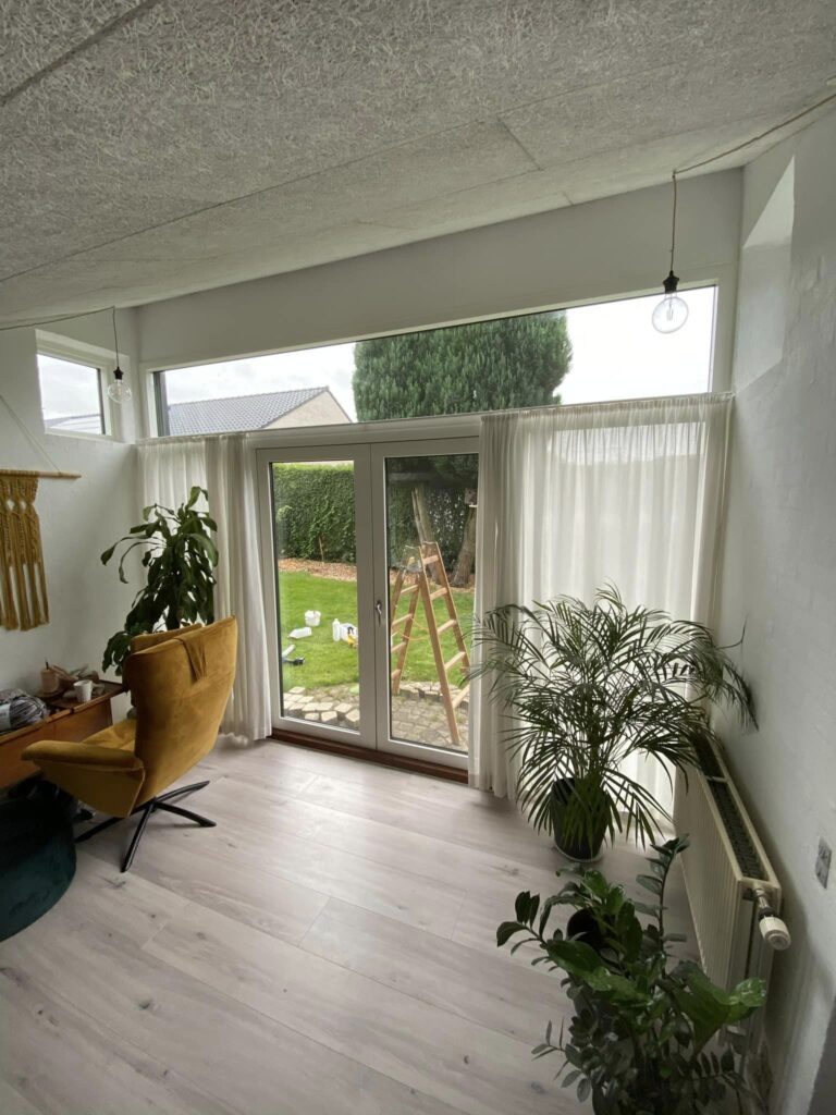 Lyst stue med store vinduer og grønne planter